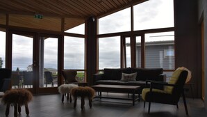 A spacious room with large windows, a sofa, a coffee table, and two fluffy stools.