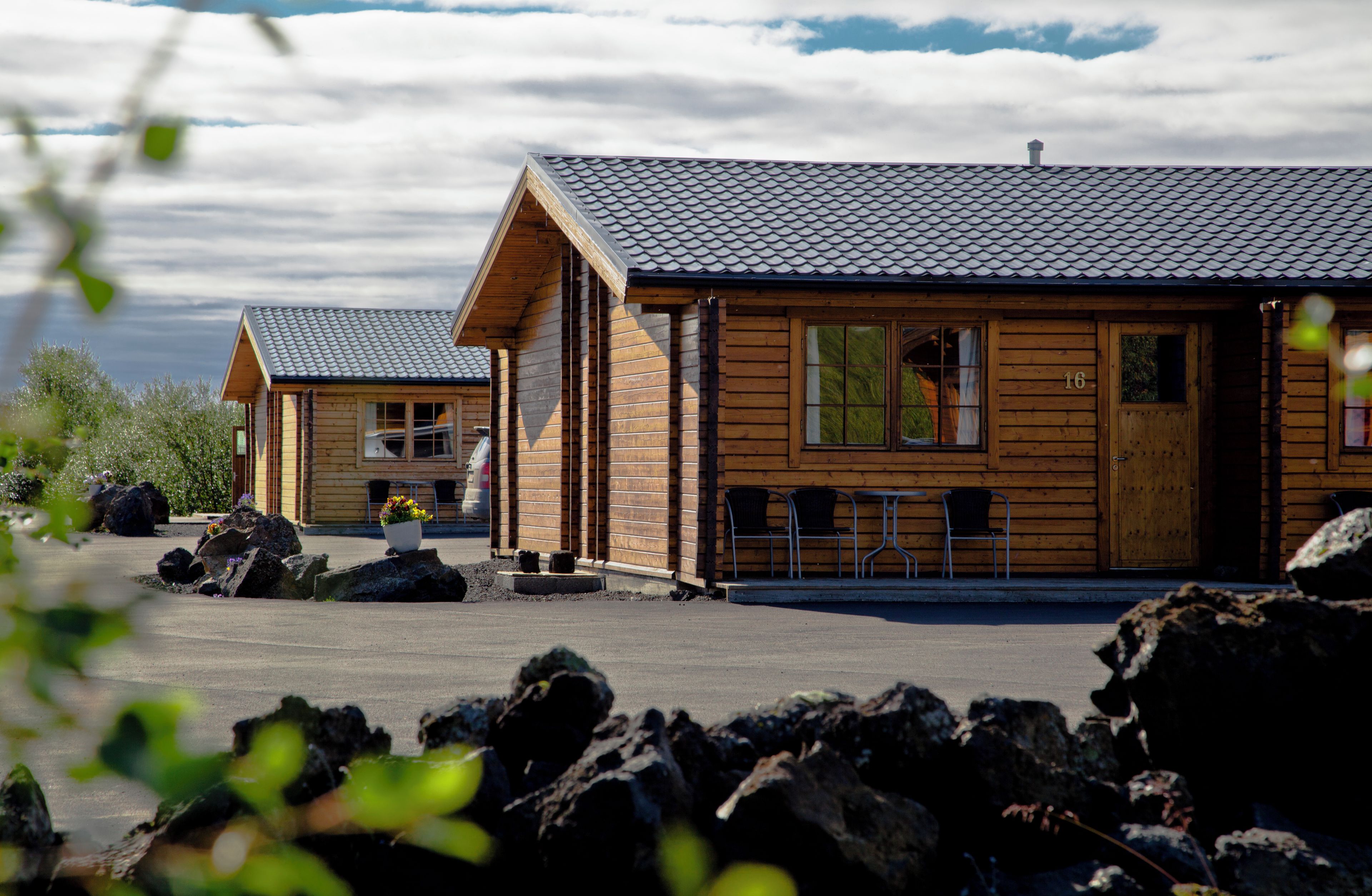 A wooden cabin with a tiled roof, a porch with chairs, and a number '16' on the door.