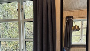 A bedroom with a large window, a bed with a patterned blanket, a bedside table, and a mirror reflecting the room. - Vogafjós Farm Resort (Myvatn)