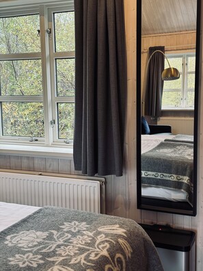 Un dormitorio con un ventanal grande, una cama con colcha estampada, una mesita de noche y un espejo que refleja la habitación.