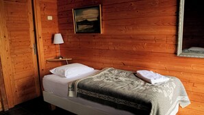 A wooden cabin room with a bed, a nightstand, a lamp, and a painting on the wall. - Vogafjós Farm Resort (Myvatn)