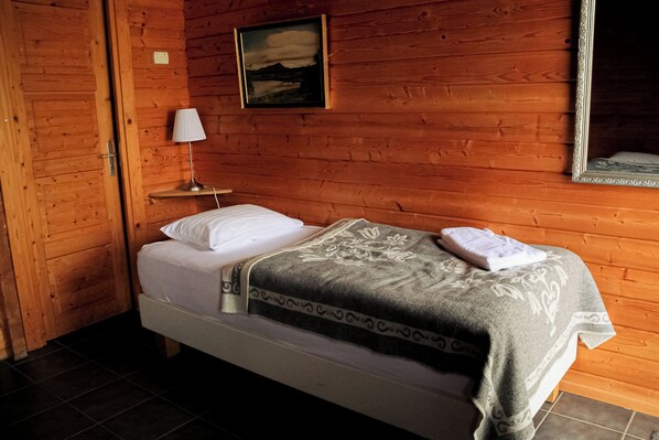 A wooden cabin room with a bed, a nightstand, a lamp, and a painting on the wall. - Vogafjós Farm Resort (Myvatn)