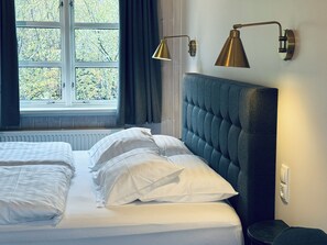 A bedroom with a bed, two bedside lamps, a window with curtains, and a radiator. - Vogafjós Farm Resort (Myvatn)