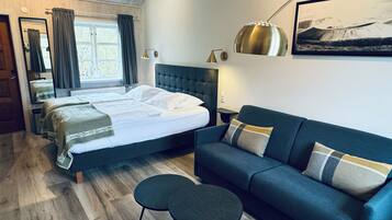 A bedroom with a double bed, a blue sofa, a small table, a lamp, and a framed picture on the wall.