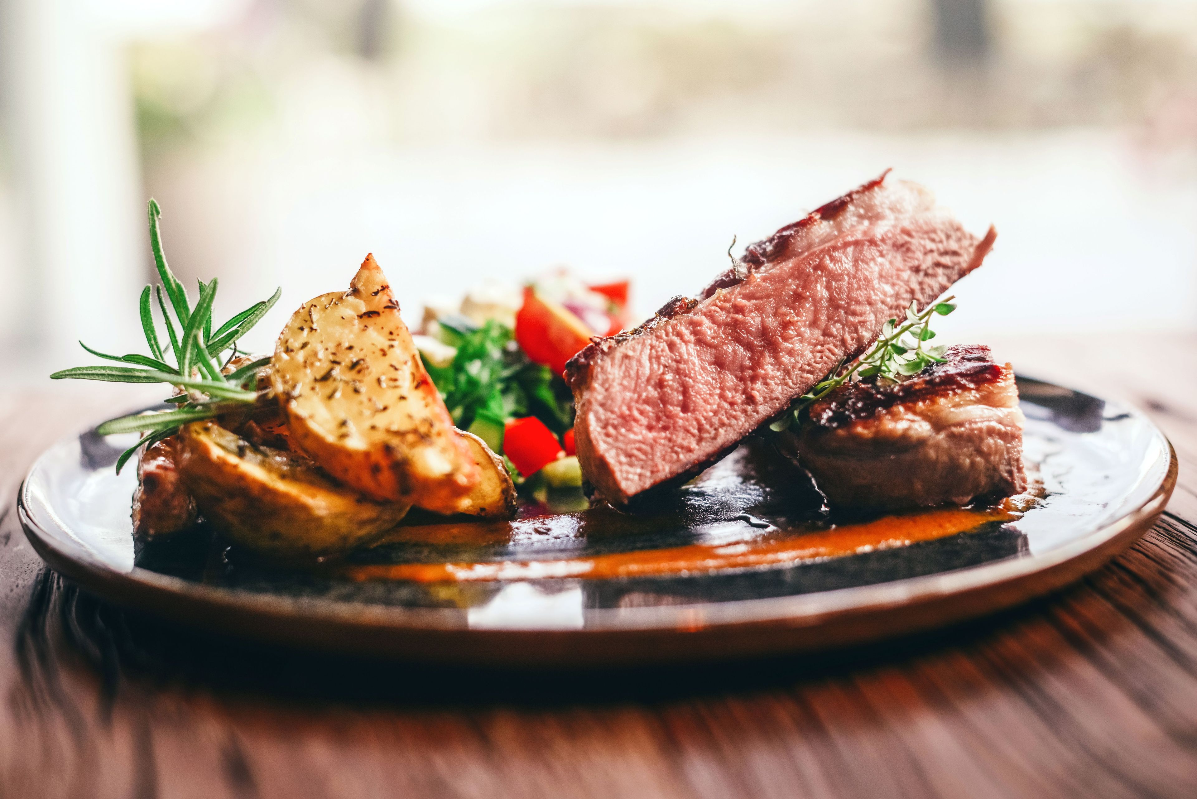 A plate with roasted meat, potatoes, and a garnish of herbs.