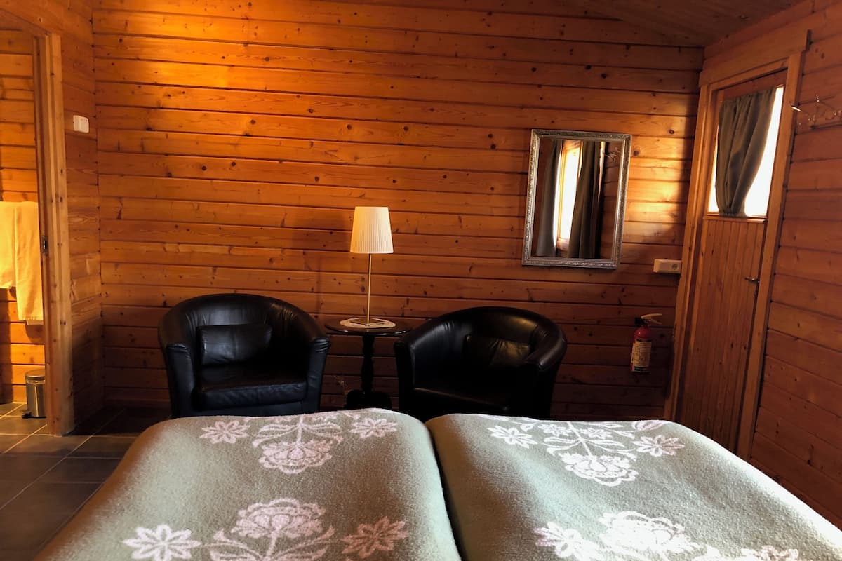 Et værelse i en træhytte med to læderstole, et lille bord, en lampe og et spejl på væggen.