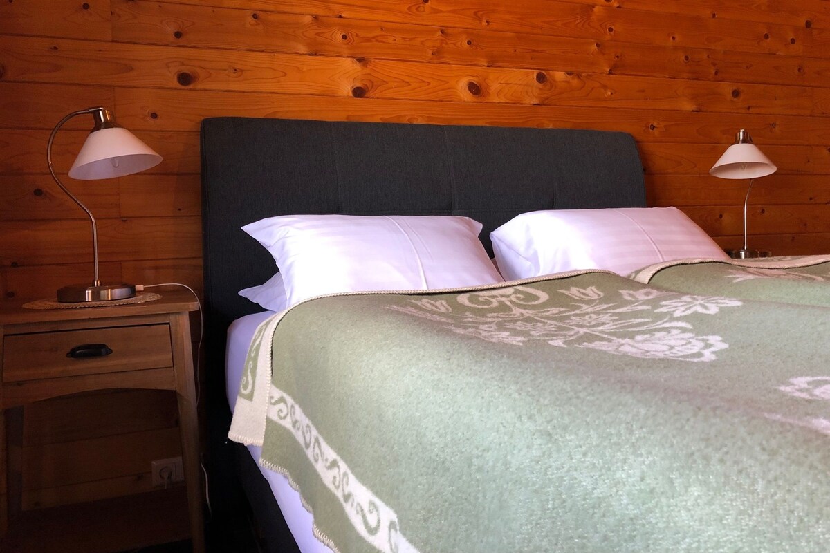 Ein Zimmer mit Holzwandverkleidung, einem Bett, zwei Nachttischlampen, einem Nachttisch und einer Schublade.