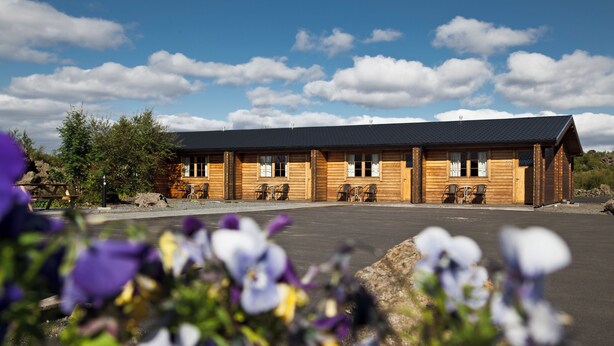 A wooden lodge with a flat roof, multiple windows, and outdoor seating. - Vogafjós Farm Resort (Myvatn)