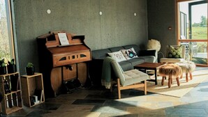 A modern living room with a piano, sofa, and a small stool. - Vogafjós Farm Resort (Myvatn)