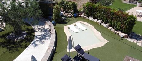 A backyard with a swimming pool, lounge chairs, and a small deck area.