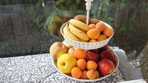 Una exposición de frutas con plátanos, manzanas y melocotones sobre un mantel estampado.