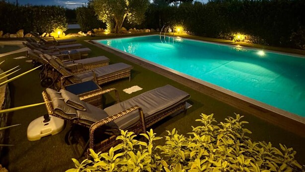 Una piscina con sillas de descanso y un jardín iluminado al anochecer.