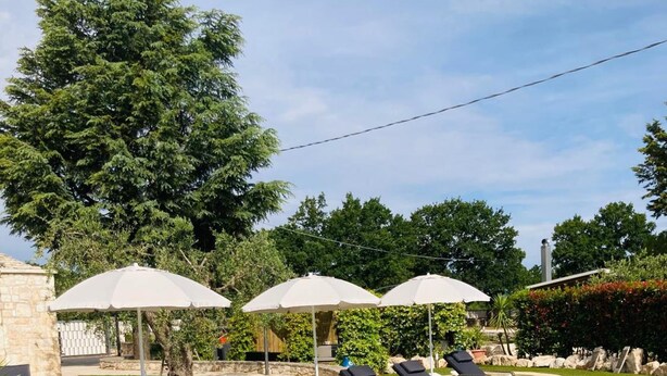 Zona de piscina con sillones de descanso y sombrillas, rodeada de vegetación y estructuras de piedra.