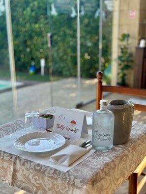 A table set with a placemat, a plate, a napkin, a glass, a bottle, a pitcher, and a sign with a landscape design. - La Linea Dell Orizzonte (Martina Franca)