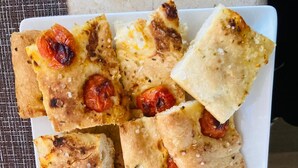 Un plato rectangular blanco con varios trozos cuadrados de pan plano cubiertos de tomates y hierbas.
