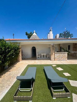 A building with a tiled roof, a covered patio area, and two lounge chairs on artificial grass. - La Linea Dell Orizzonte (Martina Franca)