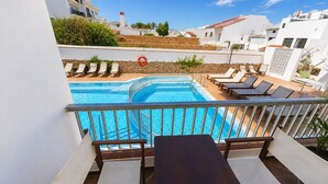 A pool area with lounge chairs and a table, surrounded by white buildings and a clear sky. - Hostal S Algaret (Mercadal)