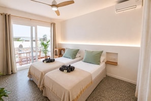 A hotel room with two beds, a ceiling fan, a small table, and a view of the outdoors. - Hostal S Algaret (Mercadal)