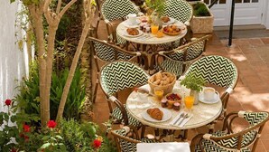 An outdoor dining area with multiple round tables and chairs, surrounded by greenery and a white wall. - Hostal S Algaret (Mercadal)