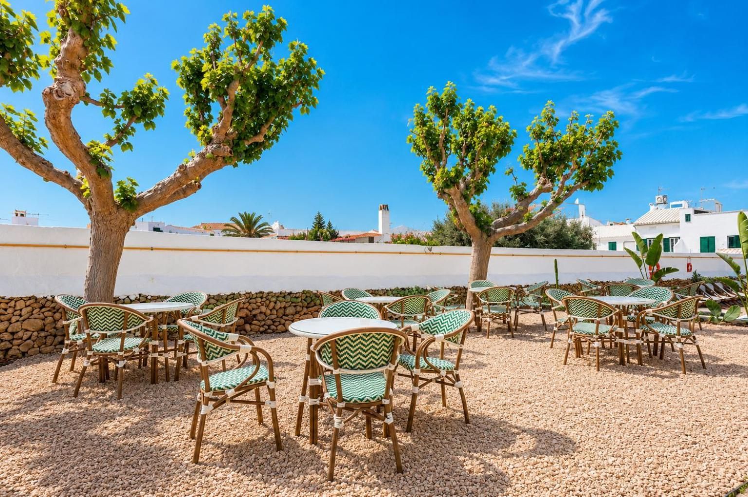 An outdoor seating area with tables and chairs, surrounded by trees and a clear sky.