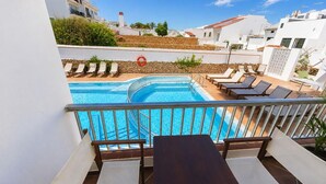 A pool area with lounge chairs and a table, surrounded by white buildings and a clear sky. - Hostal S Algaret (Mercadal)