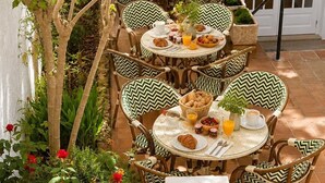 An outdoor dining area with multiple round tables and chairs, surrounded by greenery and a white wall. - Hostal S Algaret (Mercadal)