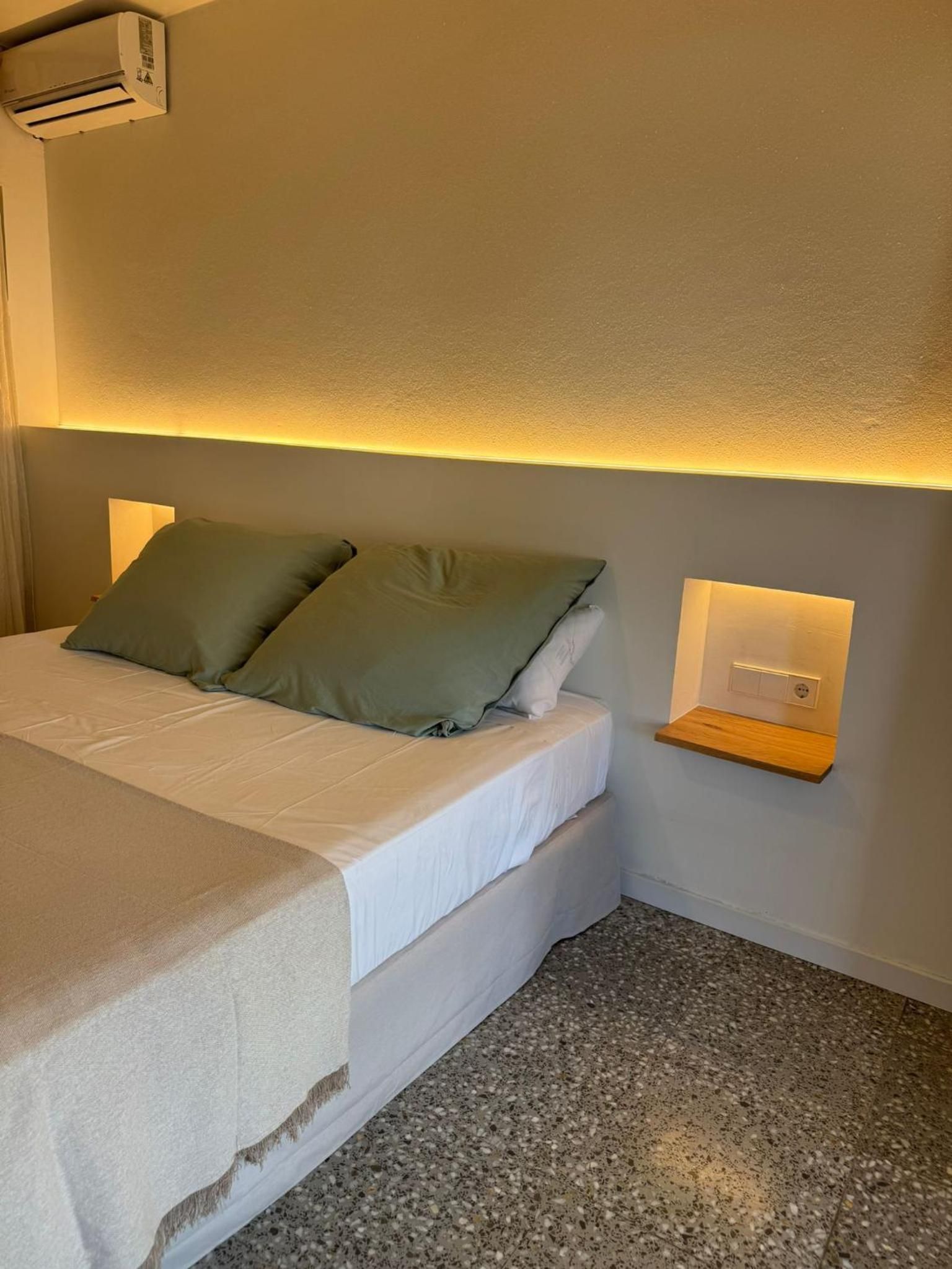 A bed with a headboard, a bedside table with a light, and a wall-mounted air conditioner.