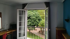 A room with a bed, a desk with a computer, a chair, and an open window with a view of greenery. - Hotel La Campana (Llanera)