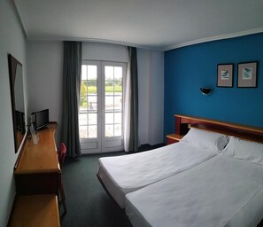 Een hotelkamer met een tweepersoonsbed, een bureau met stoel, een televisie en een groot raam met gordijnen.
