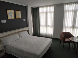 Ein Hotelzimmer mit einem Bett, einem Sessel, einem Tisch und zwei gerahmten Bildern an der Wand.