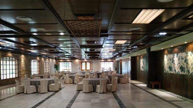 A spacious banquet hall with multiple round tables and chairs, stone walls, and large windows. - Hotel La Campana (Llanera)