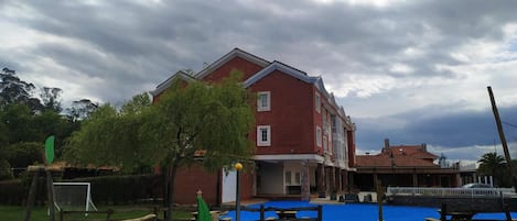 A red brick building with a flat roof, surrounded by a blue play area with wooden structures and a rope bridge.