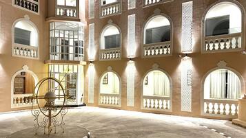 Un amplio patio con varios ventanales arqueados y balcones, una zona de recepción y una escultura decorativa de metal.