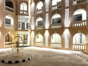 A spacious courtyard with multiple arched windows and balconies, a reception area, and a decorative metal sculpture.