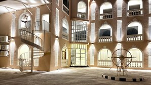 Um interior espaçoso com uma escadaria central, várias janelas em arco e uma escultura metálica decorativa.