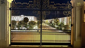 Uma entrada fechada com trabalhos em metal ornamentados e uma placa com o emblema de um sol.