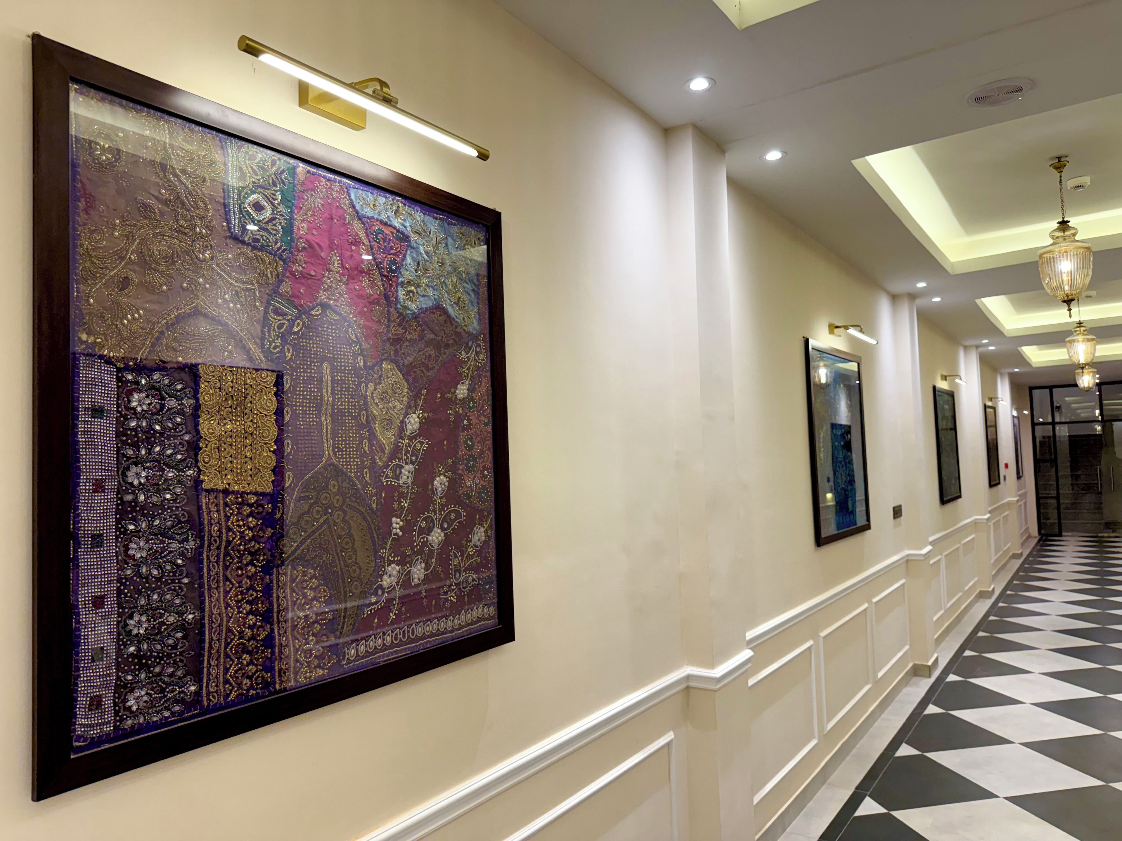 A hallway with a large framed artwork on the left, recessed lighting, and a checkered floor.