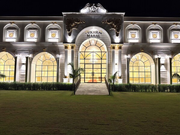A grand building with a large arched entrance, columns, and a sign that reads "PUKHRA MAHAL".