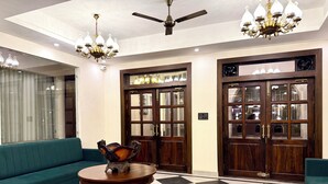 A lobby with a checkered floor, a round wooden table, a green sofa, and a chandelier.