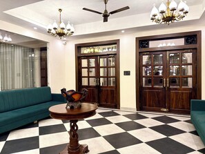 A lobby with a checkered floor, a round wooden table, a green sofa, and a chandelier. - Rambagh Resorts By Stotrak, Gwalior (Gwalior)