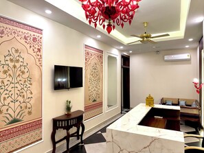 A modern hotel lobby with a marble reception desk, a flat-screen TV, decorative wall panels, a ceiling fan, and a seating area with cushions. - Rambagh Resorts By Stotrak, Gwalior (Gwalior)
