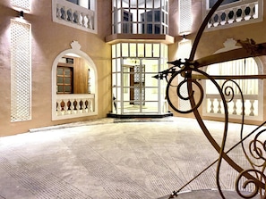 Um hall amplo com balcão de recepção, porta de entrada de vidro e grades metálicas decorativas.