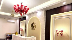 Uma área de recepção de hotel com balcão de mármore, um candelabro e um brasão na parede.