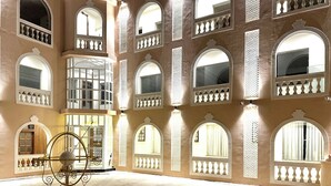 A spacious courtyard with multiple arched windows and balconies, a reception area, and a decorative metal sculpture.