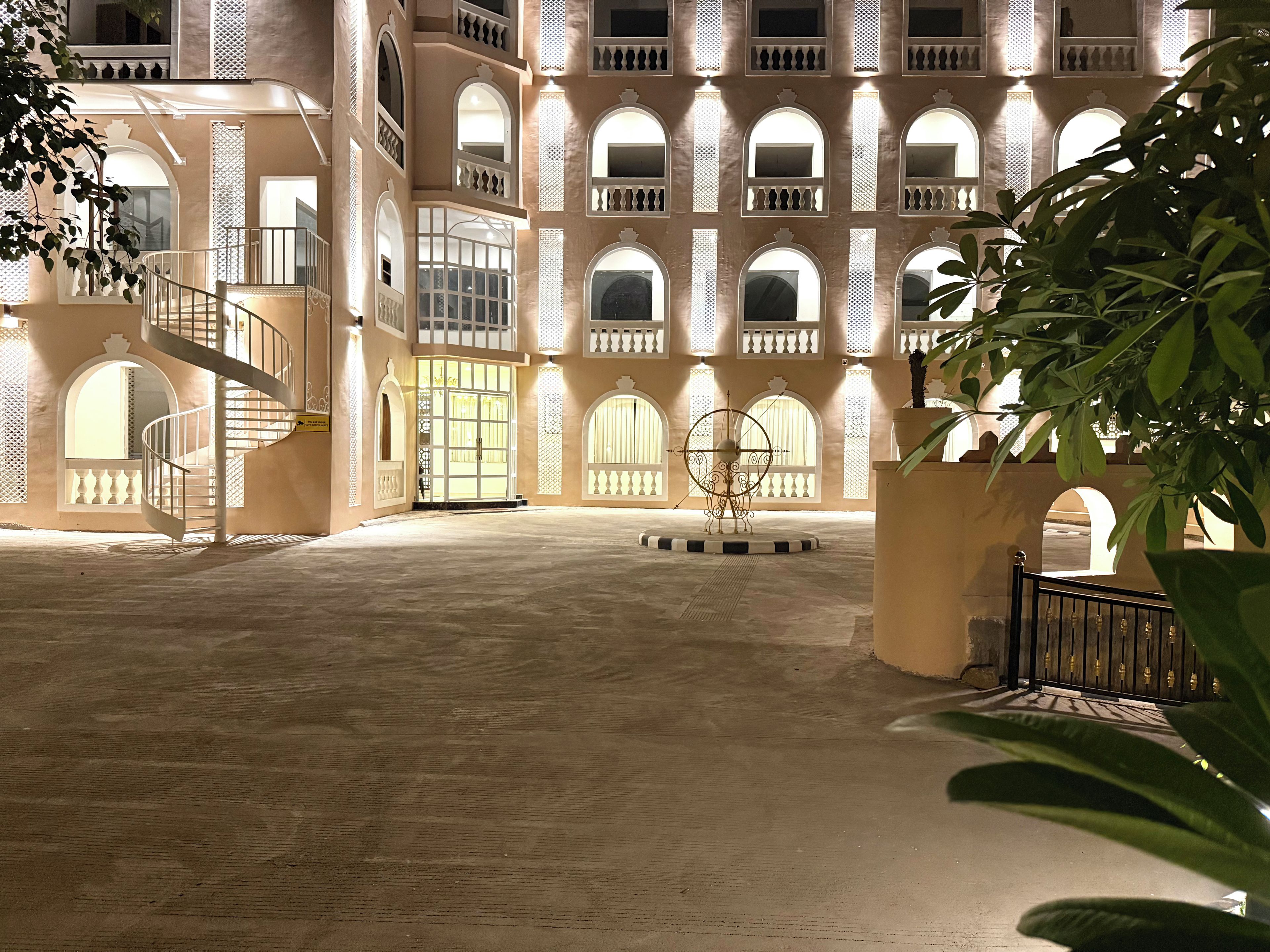 A courtyard with a spiral staircase, a large central door, and a decorative metal sculpture.