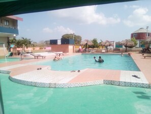 Una piscina con gente, rodeada de sillas de descanso y sombrillas.