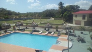 A swimming pool with lounge chairs and thatched umbrellas, surrounded by a landscaped area with a view of a hilly landscape. - Express Inn Coronado & Camping (Nueva Gorgona)