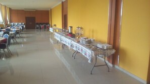 Una larga mesa de comedor con sillas, un montaje tipo bufé y una pared amarilla.
