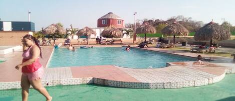 A swimming pool with a tiled edge, lounge chairs, and a building in the background.
