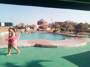 Una piscina con borde de azulejos, sillas de descanso y un edificio al fondo.